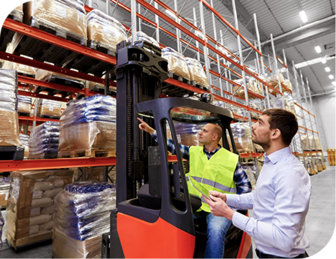 In a warehouse there are two men focused on logistics and inventory management. One, wearing a bright safety vest while operating a red forklift, looking up towards the racks filled with pallets of wrapped goods. The other, in business casual attire with a tablet in his hands, looks up to the stock. The place has a large storage capability, with shelves reaching high into the space.
